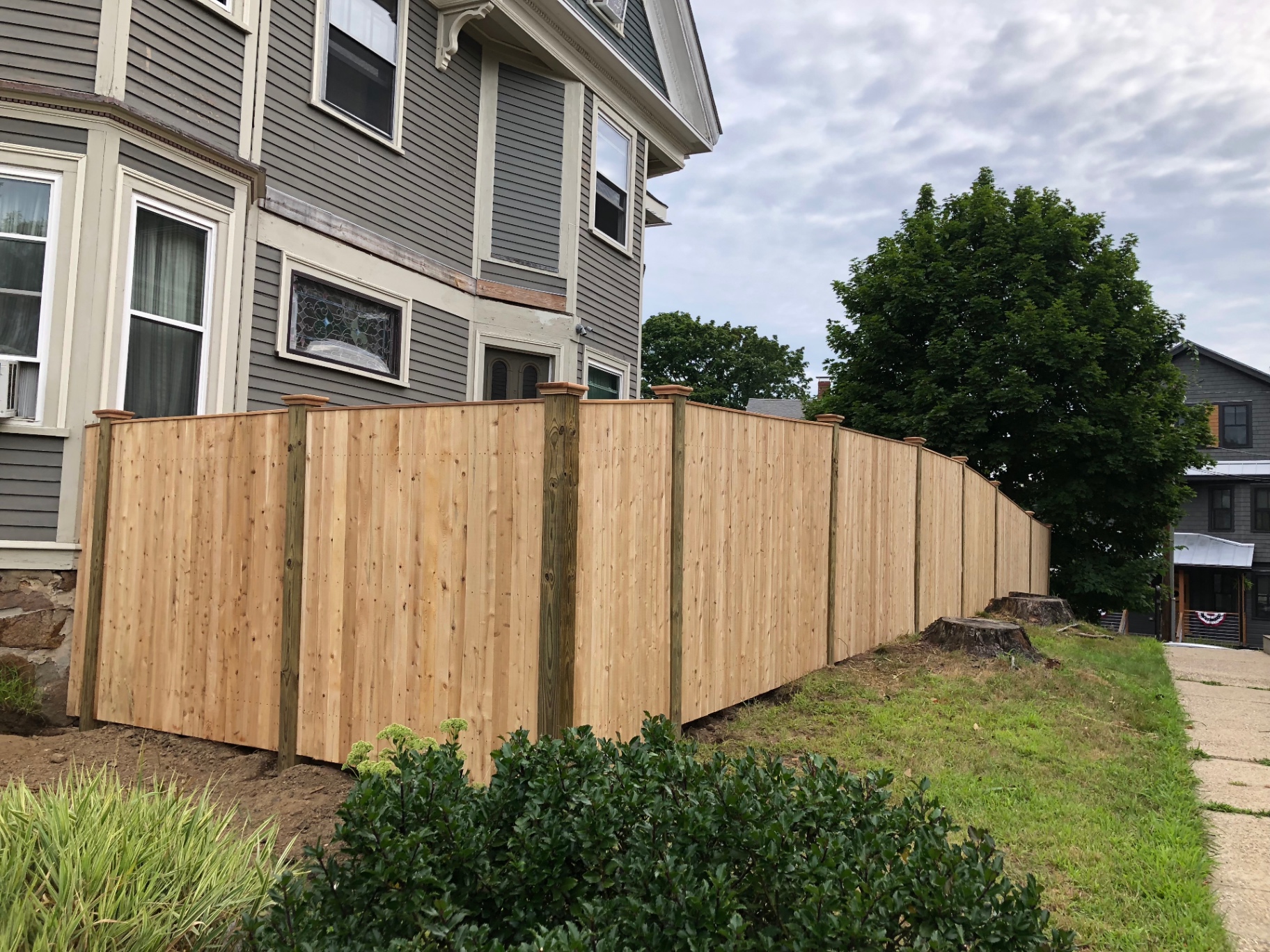 Cedar board fence with post caps installed along a Victorian home
